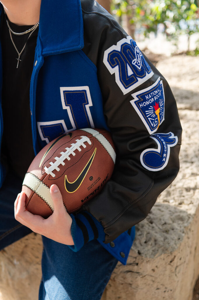 Close up shot of a senior guy holding a football wearing a high school letterman