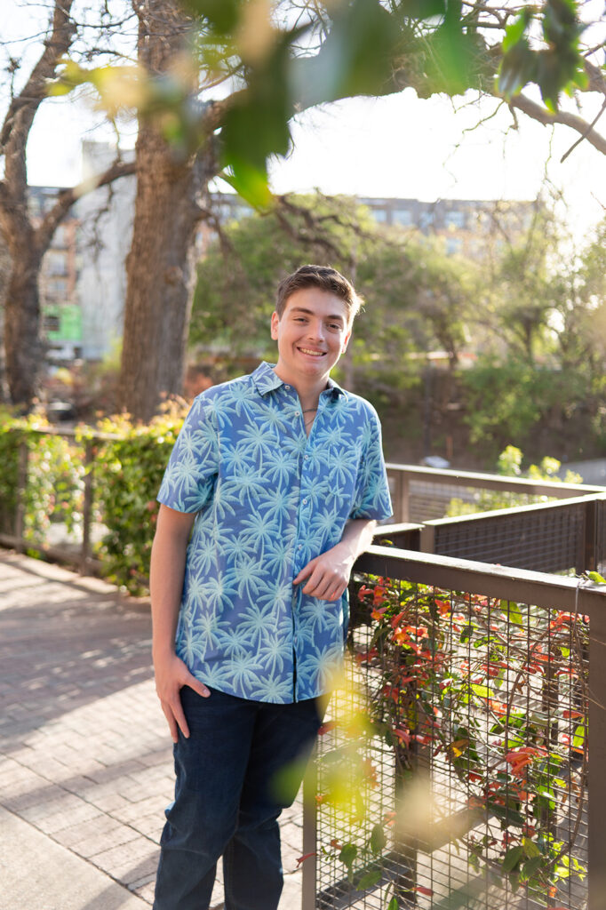Guy in a blue shirt leaning on a metal railing smiling at the camera. 