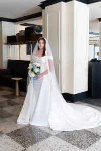 Classic Bridal Portrait of a Bride. It is a full body shot, holding flowers, and with the veil falling down her back.