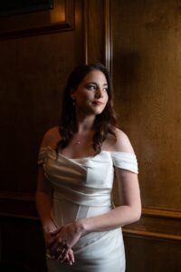 Moody Portrait of Bride leaning on a wood panel wall looking out towards a window. 