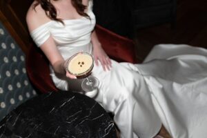 Bride sitting in her white dress while holding an espresso martini.